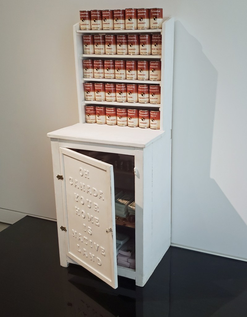 Judy Chartrand. Cupboard of Contention (2001) Slip-cast, low-fire clay, underglaze, glaze, lustre, antique cupboard, wooden letters, paint. 142.3 x 57.2 x 45.7 cm. Rennie Collection. Photo: Alina Ilyasova.